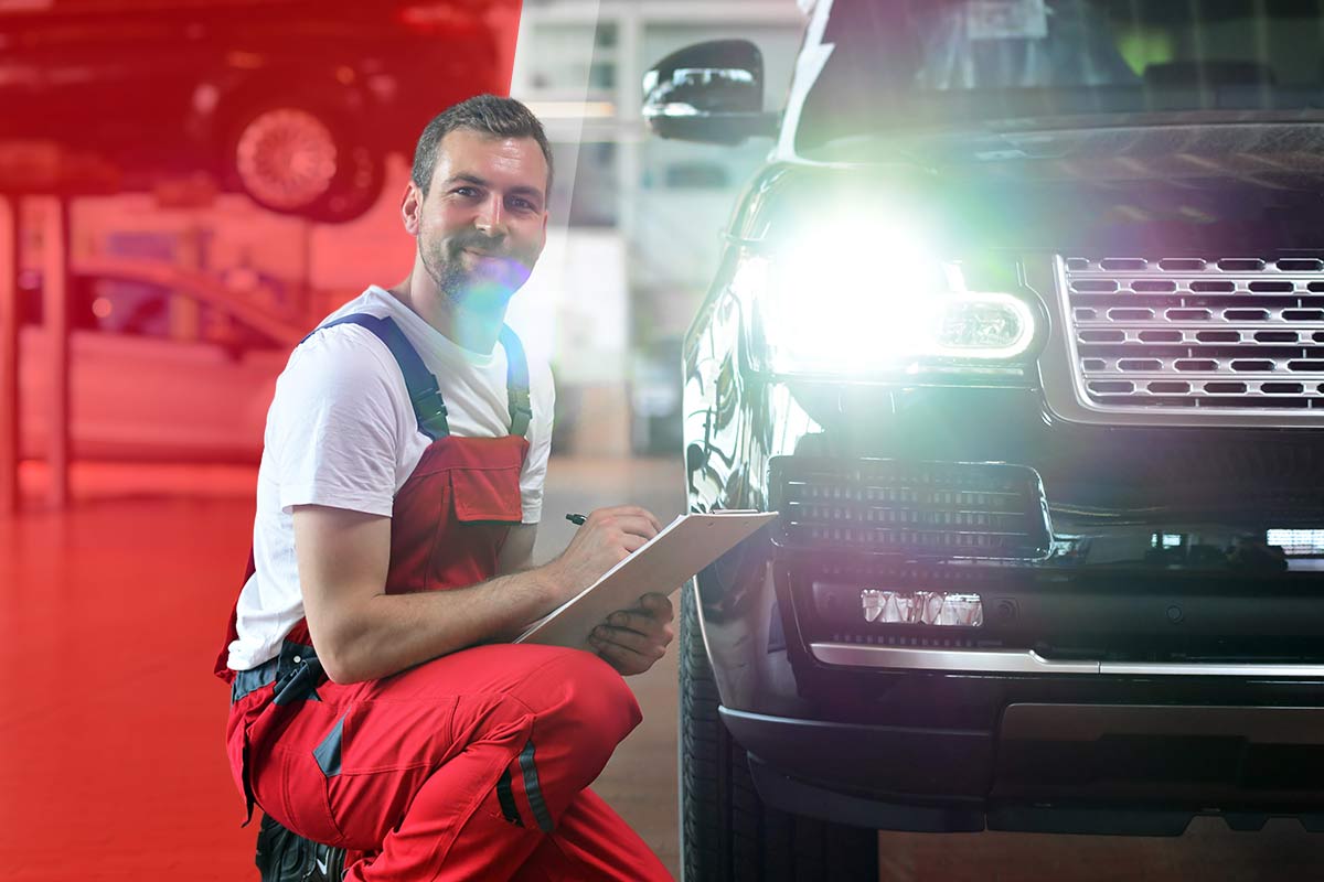 Bild zeigt einenTüv Mitarbeiter neben einem Auto beim Lichttest